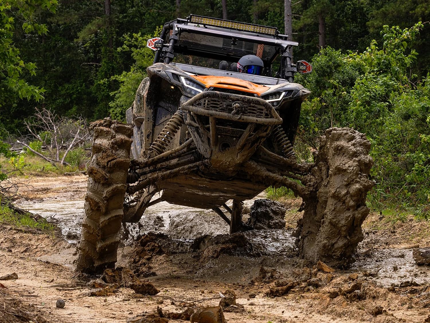 UTV on tall narrow Assassinator tires straddling a log, showing ground clearance under the machine